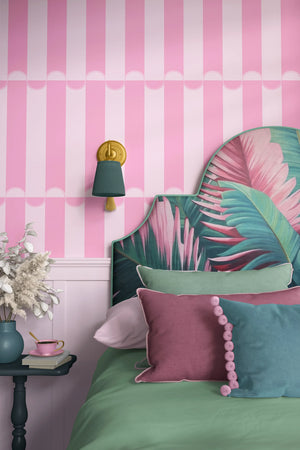 Scallop Lane wallpaper by Liberty James Studio in pink, scalloped stripes behind a bed