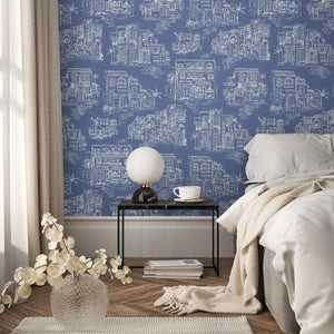 Charming Lanes wallpaper by Brand McKenzie in blue, toile-style townhouses on a bedroom wall