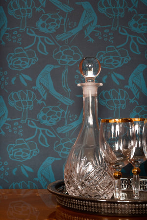 Chattering of Choughs wallpaper by Annika Reed in teal, choughs among leaves above a sideboard