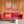 Deco Prism wallpaper by Liberty James Studio in orange, art deco wave stripes behind a sofa in a living room