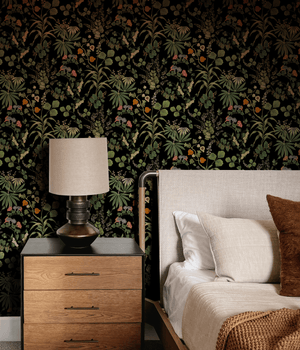Little Eden wallpaper by Deus ex Gardenia in black, lush leaves and fruit behind a bed