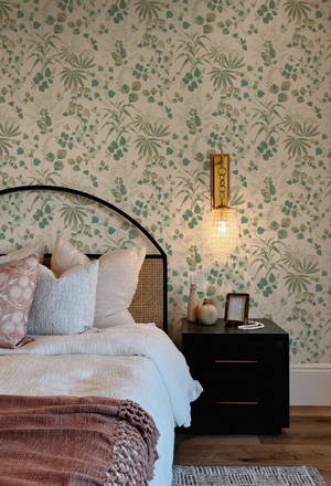 Little Eden wallpaper by Deus ex Gardenia in cream and green, lush leaves and fruit behind a bed