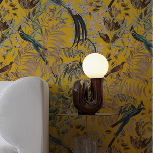 Resplendent Woods in India wallpaper by Deus ex Gardenia in yellow, parrots in tropical branches in a styled room setting