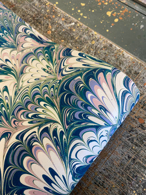 Serpentine in Spring wallpaper by House of Amitié in blue and green, partly unrolled roll showing peacock-feather marbling