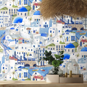 The Mediterranean wallpaper by Brand McKenzie in blue and white, a whitewashed hillside village behind a dining table
