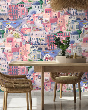 The Mediterranean wallpaper by Brand McKenzie in lilac and pink, a whitewashed hillside village behind a dining table