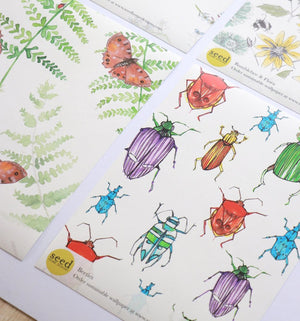 Beetle wallpaper by Seed Home Designs in red, blue and green, partly unrolled roll showing watercolour beetles