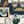 Connecting Frames wallpaper by Brand McKenzie in navy, a gallery wall of framed portraits behind a sofa in a living room
