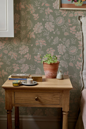 Amelie wallpaper by Curate Space in lichen green, vintage chintz florals in a room with a wooden bedside table and a plant
