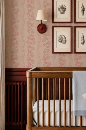 Bonnie wallpaper by Curate Space in red, seashells and seaweed in a stripe in a nursery with a wooden cot and framed shell prints