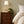 Elsie wallpaper by Curate Space in lichen green, dried poppy head motifs in a bedroom with a wooden bedside chest and table lamp