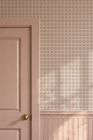 Mabel wallpaper by Curate Space in soft pink, small rosette motifs in a hallway with a pink door and panelling