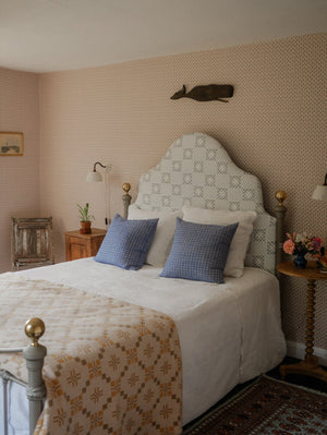 Maeva wallpaper by Curate Space in rouge red, a small trailing vine in a bedroom with an upholstered headboard