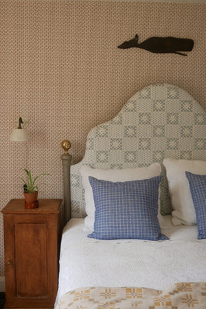 Maeva wallpaper by Curate Space in rouge red, a small trailing vine in a bedroom with an upholstered headboard and a wooden bedside table