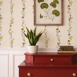 Olive wallpaper by Curate Space in light cream, vertical stripes of botanical stems and wildflowers behind a red chest of drawers and framed botanical print