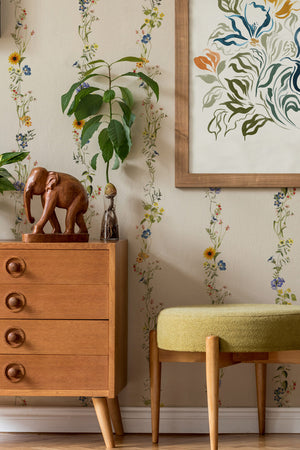 Olive Curate Space wallpaper in light cream, vertical stripes of botanical stems and wildflowers in a room with a mid-century chest, a yellow stool and a plant