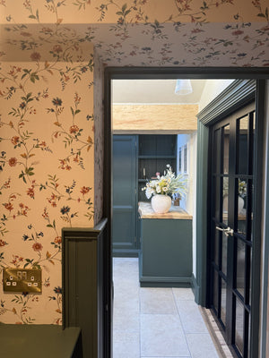Paloma wallpaper by Curate Space in off-white, trailing floral stems in a hallway looking through to a kitchen