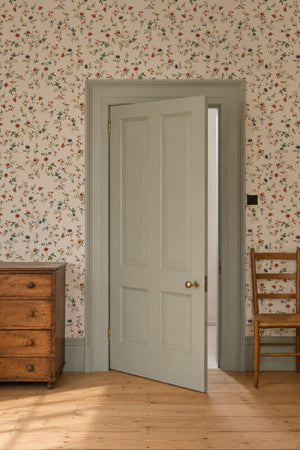 Paloma Curate Space wallpaper in off-white, trailing floral stems in a hallway with a grey-green door and a wooden chest
