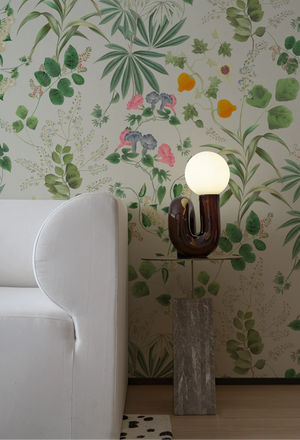 Eden wallpaper by Deus ex Gardenia in cream and green, lush leaves and fruit behind a sofa in a living room