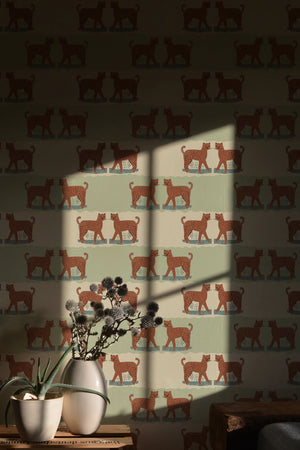 A Leopard Never Changes His Spots wallpaper by Annika Reed in cream, leaping leopards behind a sofa in a living room