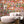 Mayhem Mansion wallpaper by Brand McKenzie in orange and pink, animals partying in a mansion behind a sofa in a living room