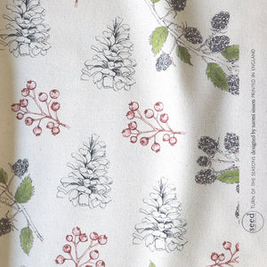 Organic Turn of the Seasons Pinecone and Berry linen by Seed Home Designs in green and red, draped, showing