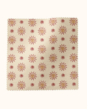 Sunshine Masquerade linen by Annika Reed in cream and red, flat sample of sun and mask motifs