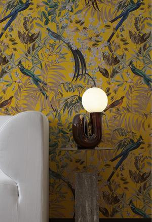 Resplendent Woods in India wallpaper by Deus ex Gardenia in yellow, parrots in tropical branches on a feature wall